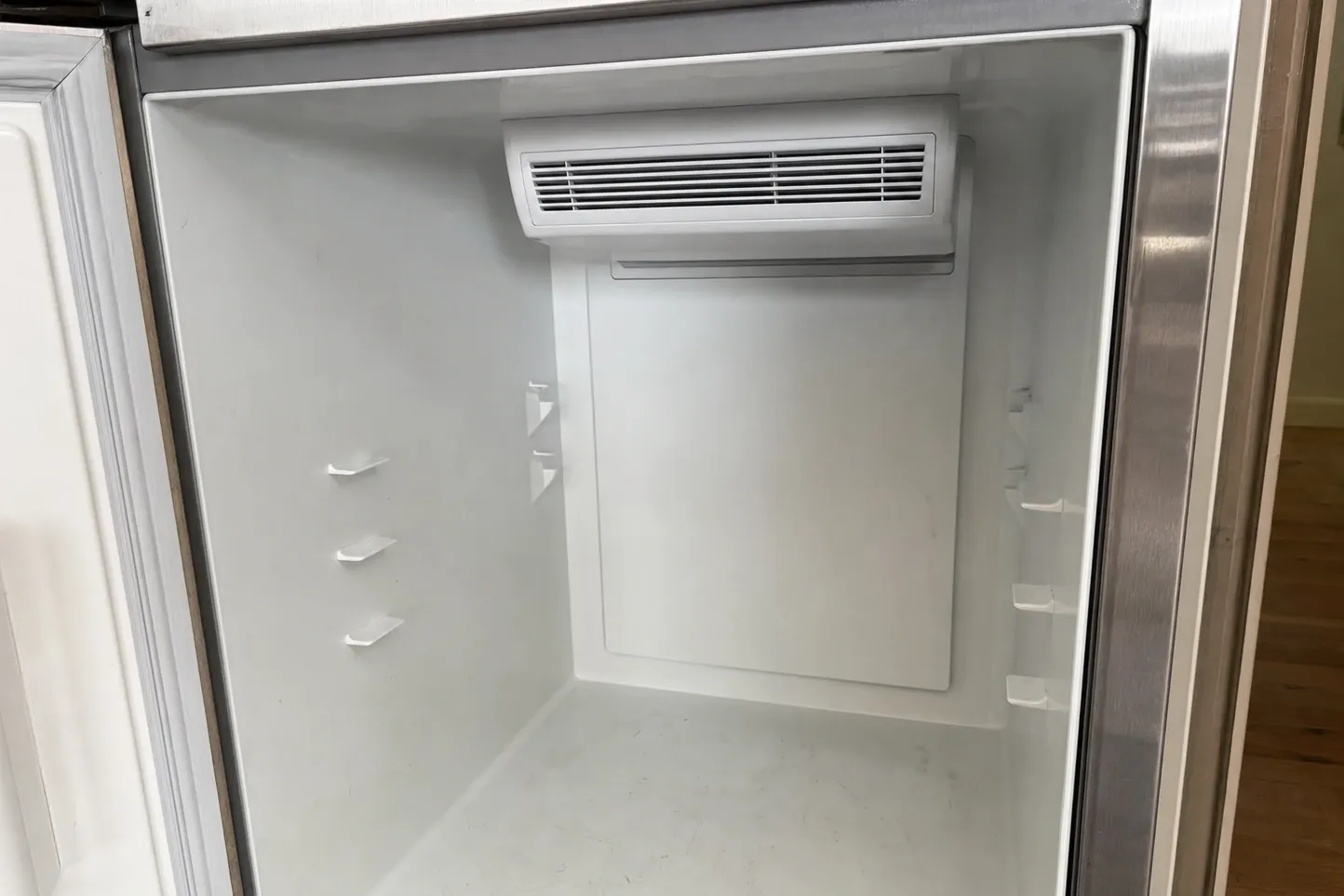 The empty interior of a built-in compartment, a moulded air outlet grille set high on the rear wall and shelf supports stepping down both side walls